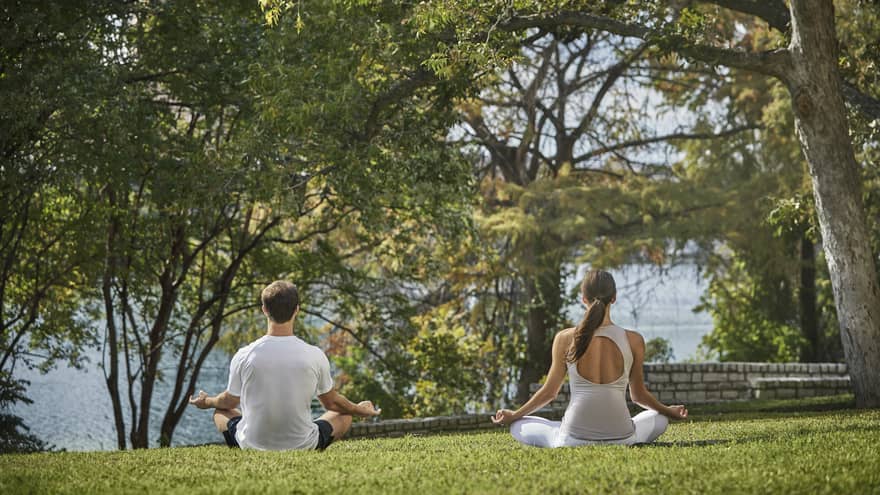 A man and woman in a yoga pose outside near trees.