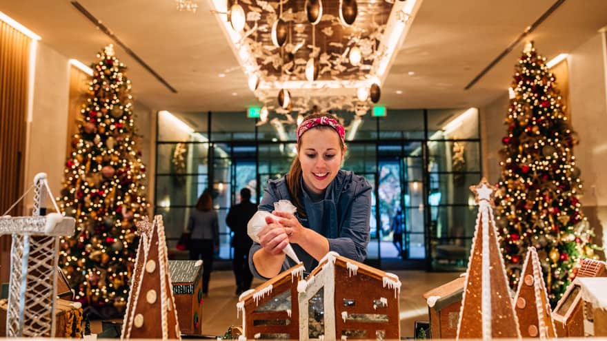 An employee carefully applies icing to an intricate gingerbread house
