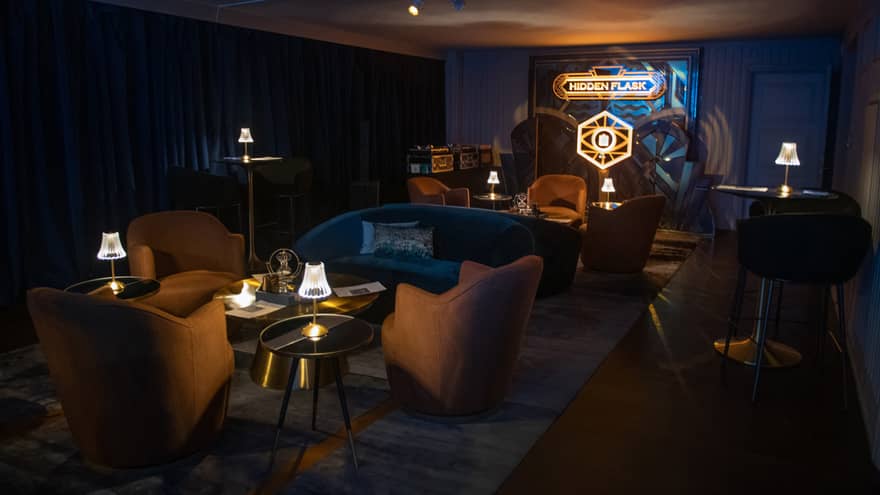 Room with couches, chairs and tables, and an illuminated Hidden Flask sign.