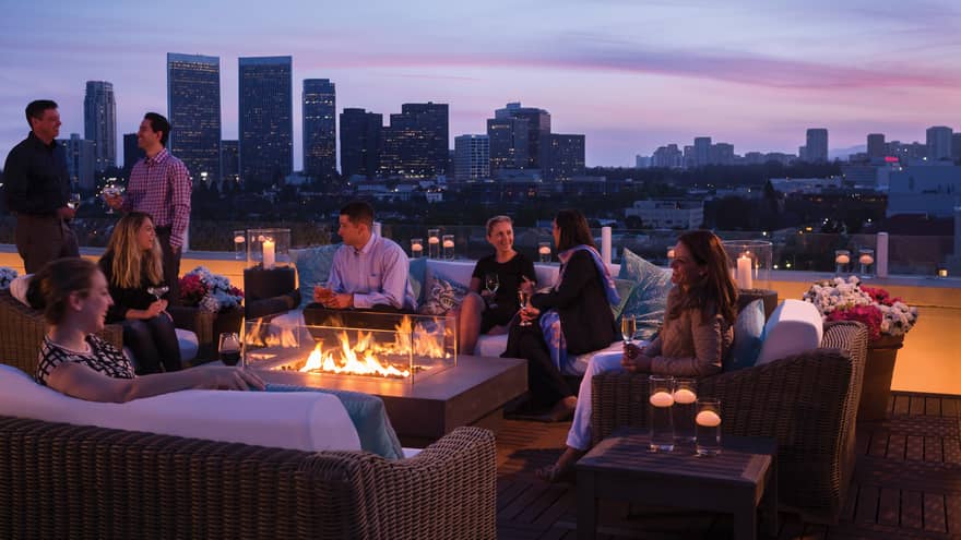 Guests socialize around outdoor fireplace Veranda Suite rooftop terrace, city views at dusk