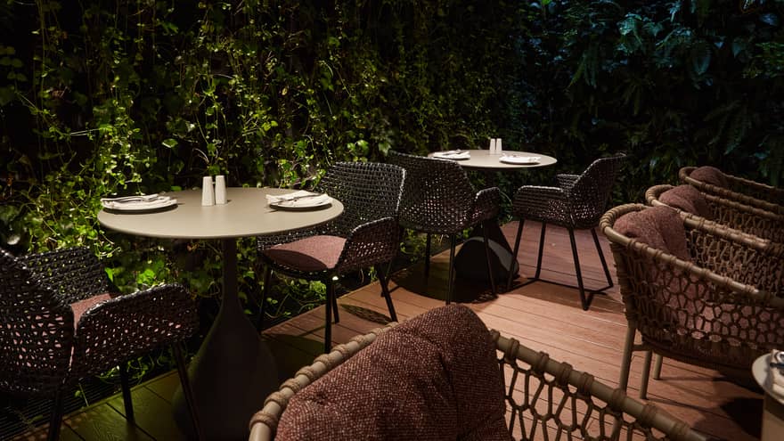 Dimly lit restaurant terrace surrounded by walls of greenery