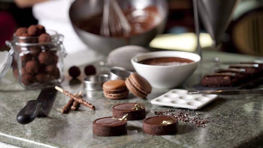 Close-up of fine chocolates, macarons, bowl of melted chocolate on counter