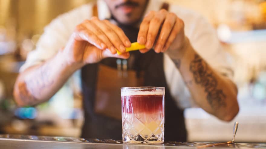 A bartender squeezes a lemon over a pink and white mixed drink. 