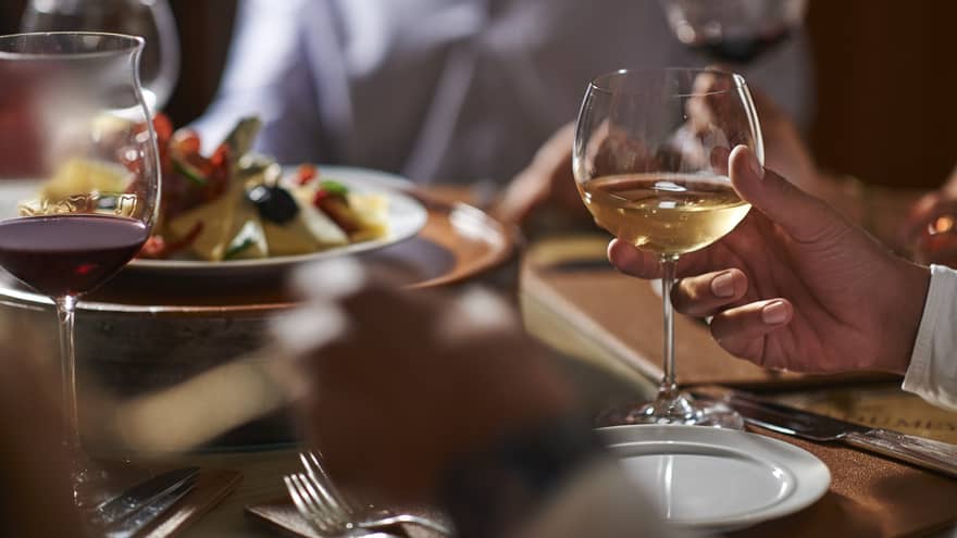 Close-up of hand holding wine glass by dinner plate on table