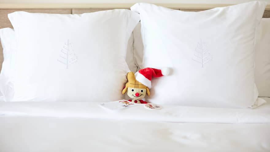 A snow man plush in a bed with white sheets.