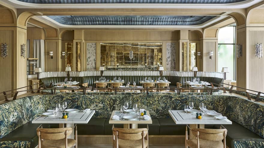 Bright, open restaurant space with neutral-coloured walls, decorative recessed ceilings, natural light, and tables and chairs and banquette seating