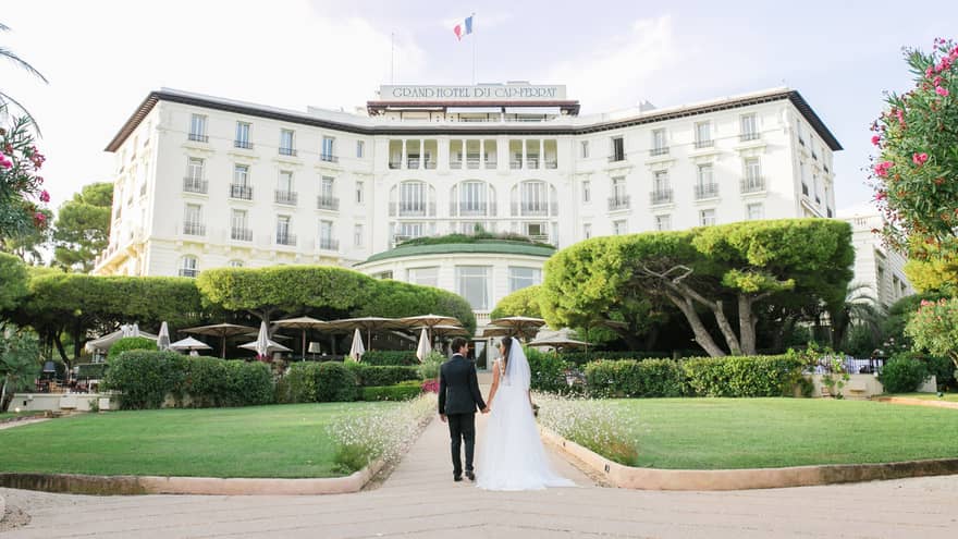 Bride and groom walk on garden path towards Four Seasons Hotel Grand-Hotel du Cap-Ferrat