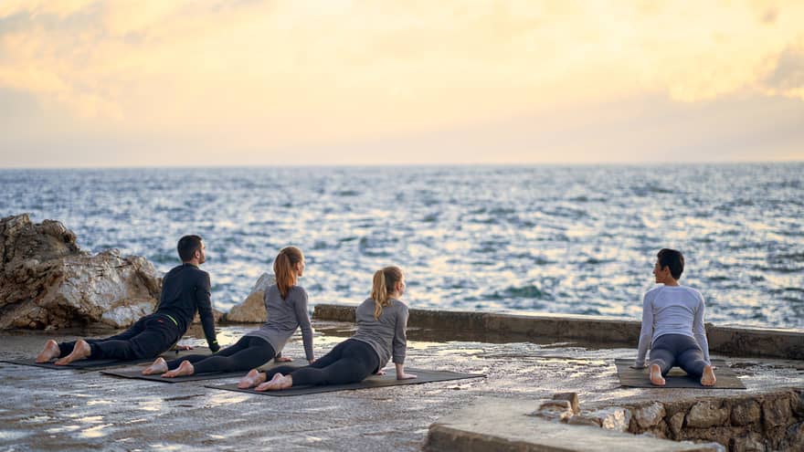 Three people and yoga instructor in upward dog pose on seaside patio at sunrise 