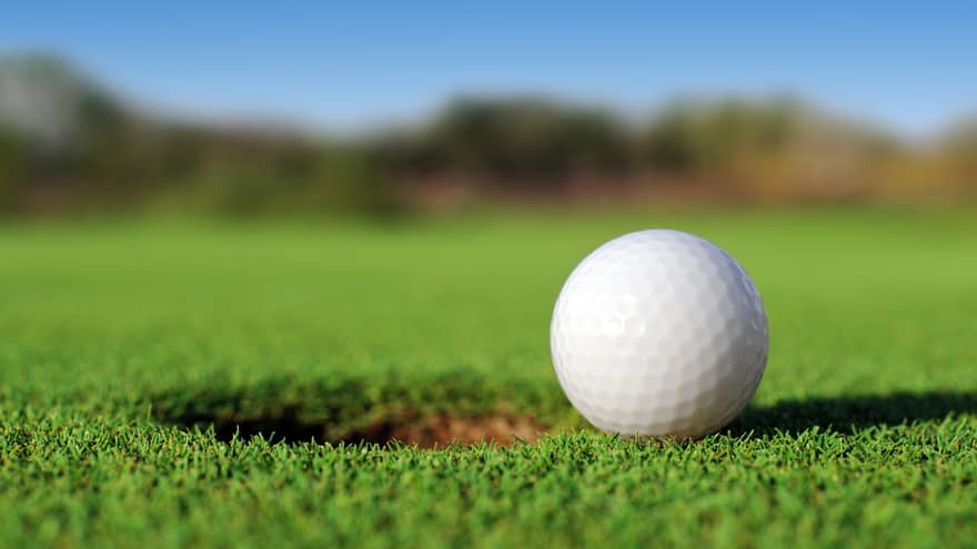 A close up of a white golf ball sitting right next to a golf hole on the course