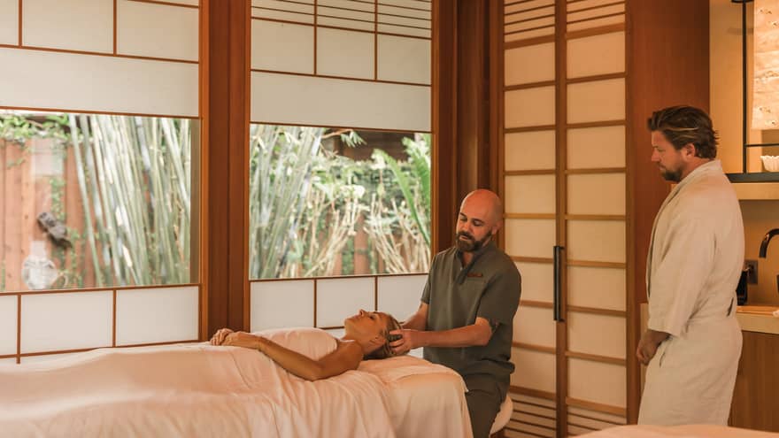 Man performs head massage on a woman laying on spa treatment table