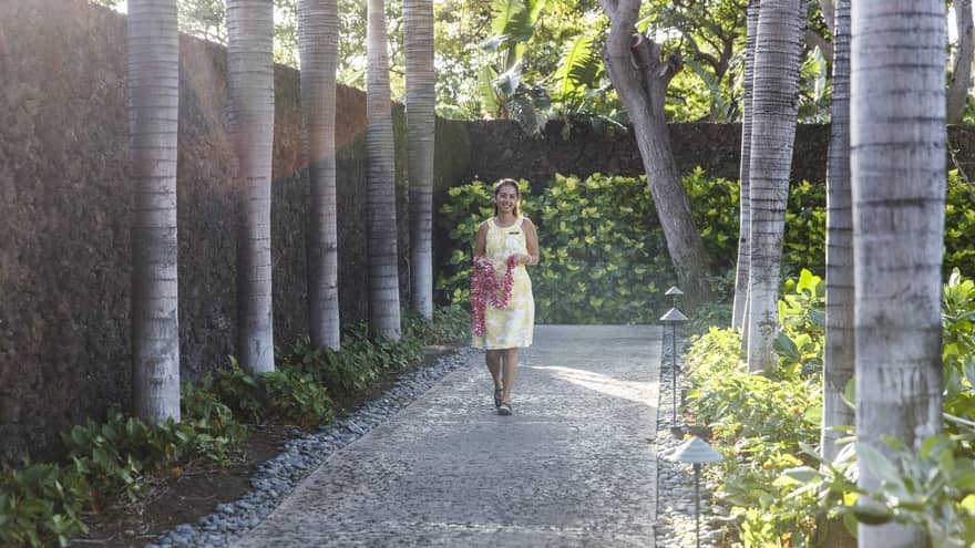 Hotel staff holding fresh flower lei necklace walks down garden path