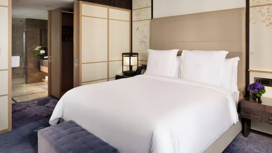 Elegant bedroom with a king-size bed, soft accent lighting, and sliding doors leading to a spacious bathroom at Four Seasons