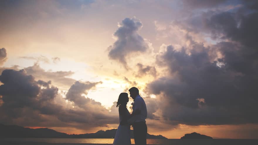 A silhouette of a man and woman embracing as the sun sets beyond them over the mountains