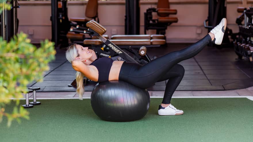 Woman does an exercise on a large exercise ball at indoor-outdoor luxury hotel gym