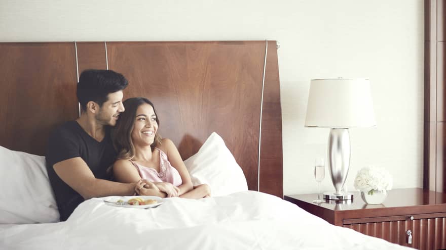 Couple cuddles in bed in modern hotel room