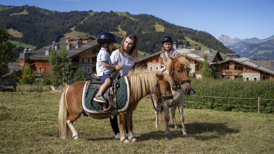 Instructor guiding two children on riding ponies with mountains in backdrop