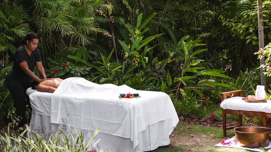 Guest receiving a massage by a massage therapist on a table set up among the foliage.