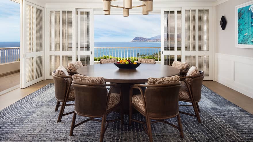 Dining room featuring a large circular table and eight chairs, and doors opening to ocean views on two sides