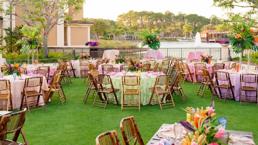OUtdoor lawn set up for a wedding reception with table rounds covered in tables clothes of varying colours including lilac, pink, green and peach