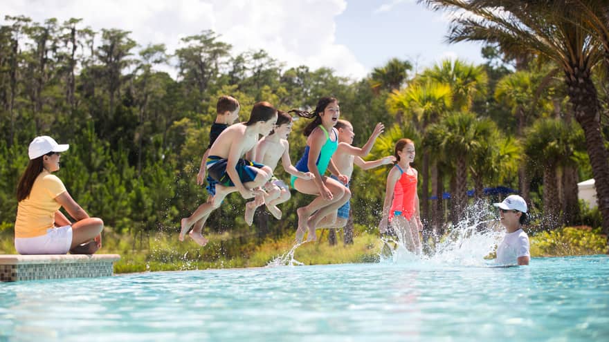 Group of children wearing swimsuits jump into outdoor swimming pool