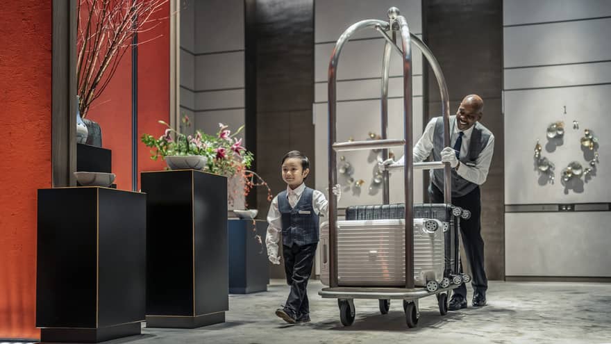 Little boy helps bellman pull luggage cart through lobby
