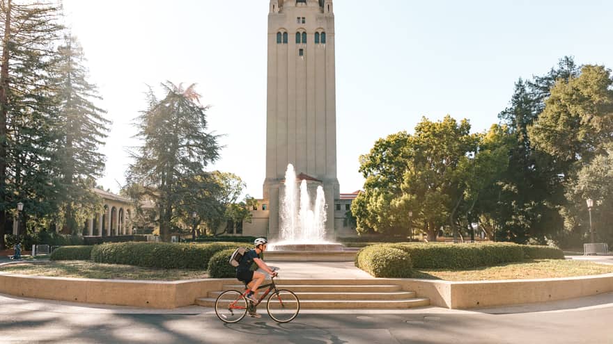 A large tower building with a biker cycling passed it in a park.