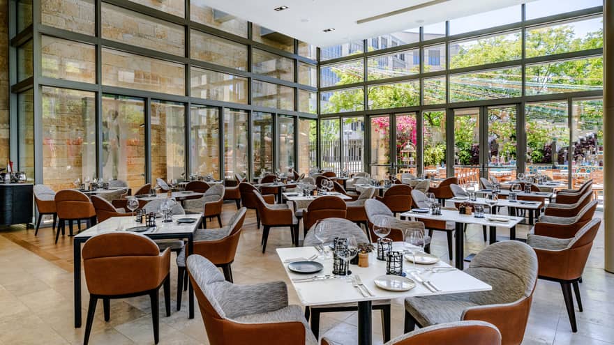 Restaurant with floor to ceiling windows and tables set with silverware and plates