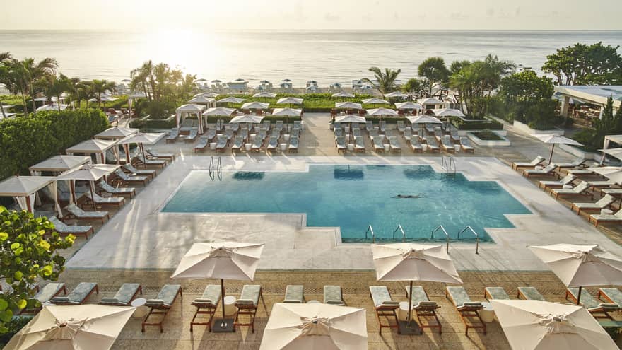 An outdoor pool near the ocean with umbrellas and lounge chairs around it.