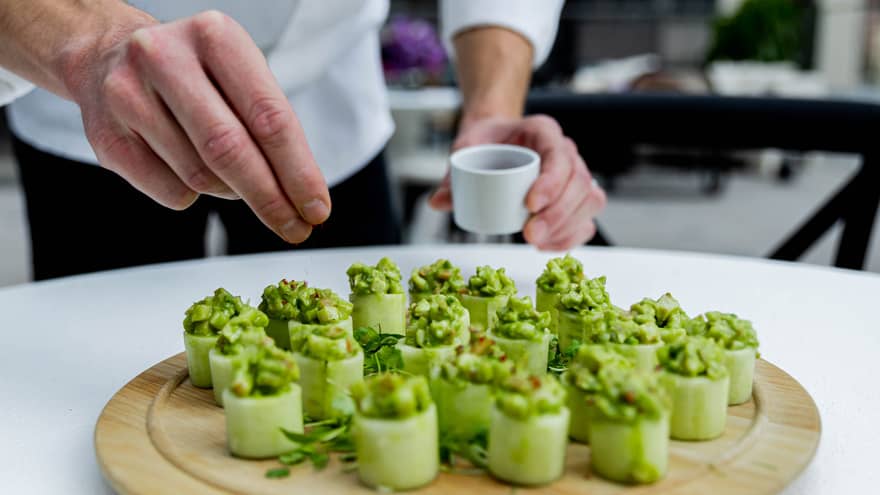 A chef seasoning a green dish made of vegetables on a wood round tray.