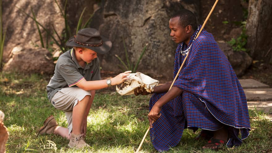 Maasai guide shows large skull to young boy wearing safari hat