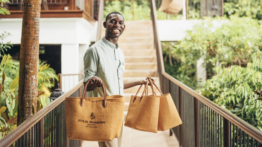 Person in linen shirt standing on catwalk holding four orange tote bags