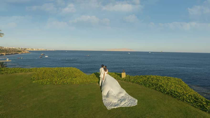 Bride and groom standing on lush green cliff overlooking the Red Sea