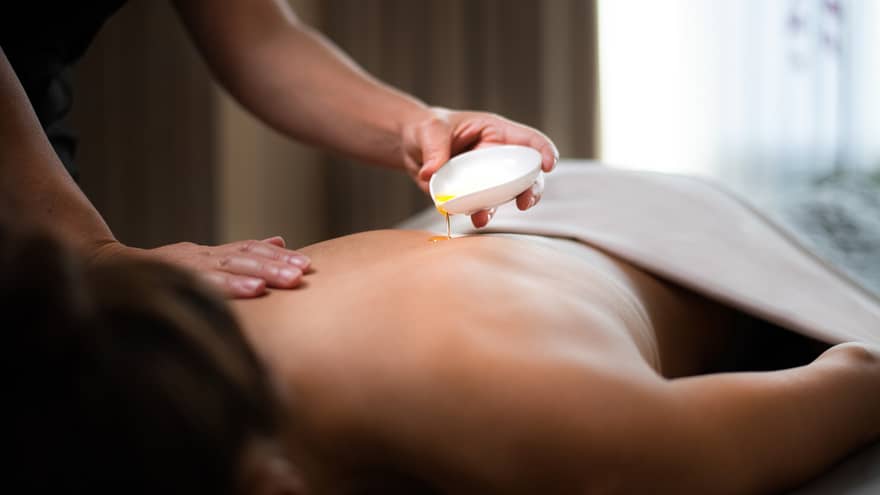 Spa staff pours hot oil on person's back during massage
