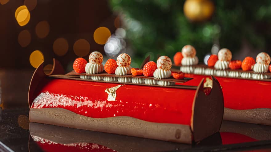 Two red yule logs topped with raspberries and chocolate trimmings