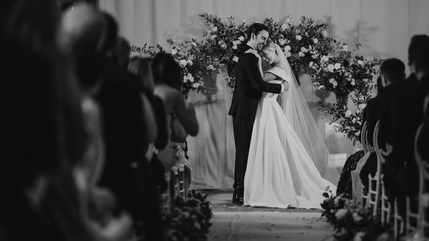 Wedding couple embraces at altar as guests on either side of the aisle look on