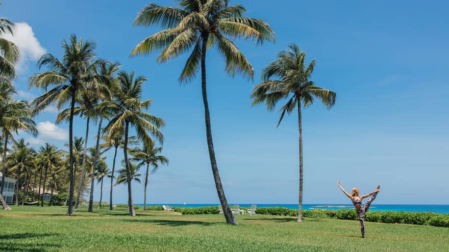 A person doing a yoga pose outside near the ocean and palm trees