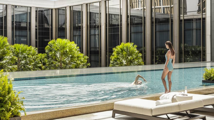 Man swims laps as woman in blue bathing suit watches poolside