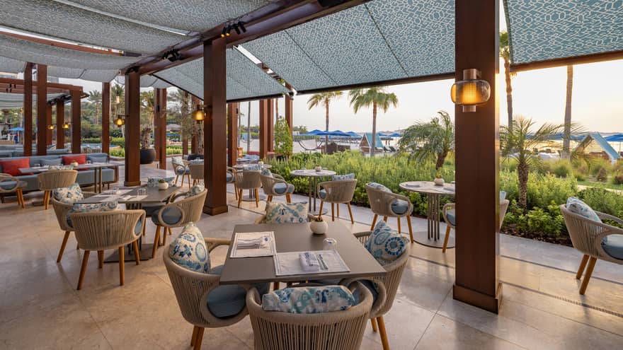 Terrace of restaurant decorated in light blues and greys that looks over a beachfront garden