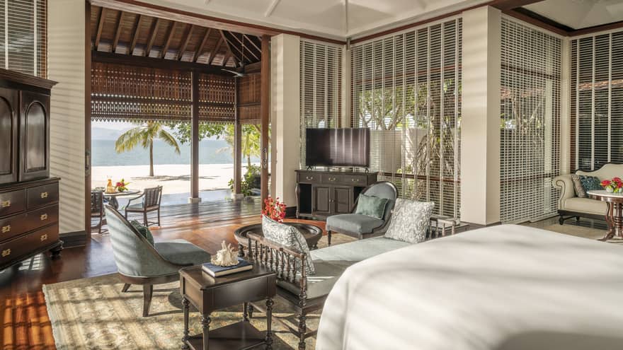 Bedroom with chaise and two arm chairs, plus opening to covered terrace and beach