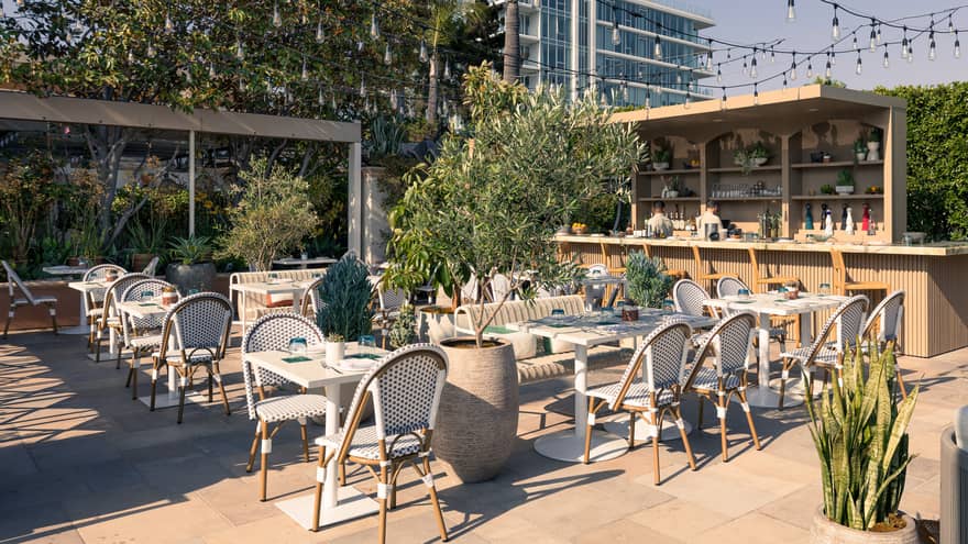 Outdoor dining patio with white tables and chairs, a bar nearby and string lights overhead