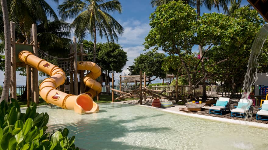 Kids Club children's pool with winding yellow water slide under palm trees