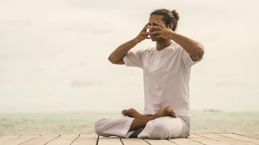 A guest peacefully practicing yoga therapy while sitting on a dock by the ocean