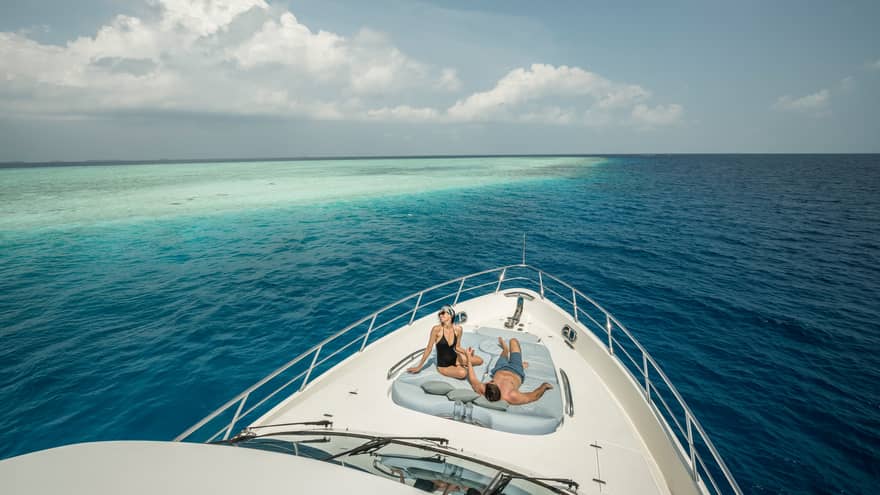 Couple lounge on cushions at front of Voavah Summer private yacht on ocean