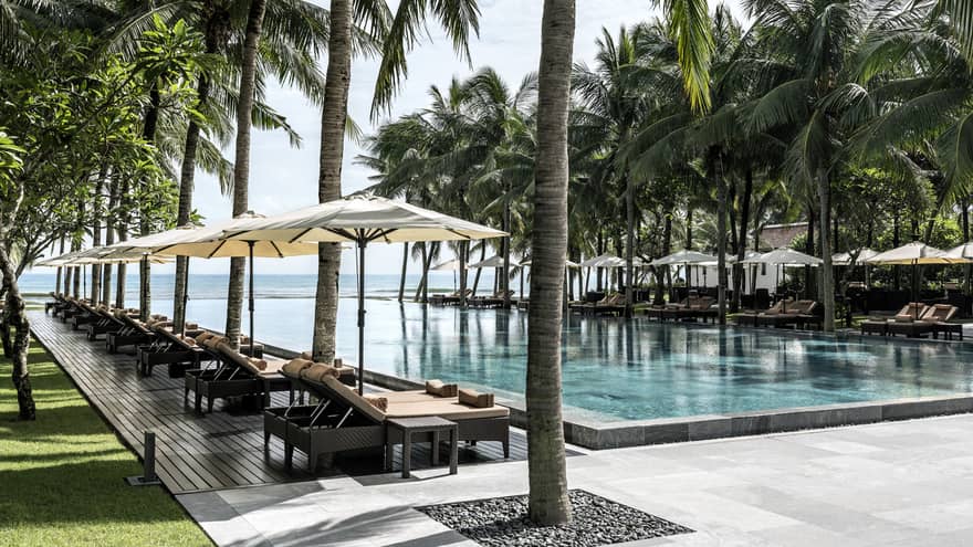 Lounge chairs, patio umbrellas, large palm trees line outdoor swimming pools