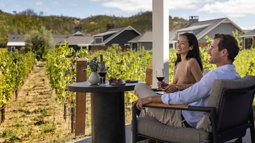 A man and woman sitting outside looking at a vineyard.