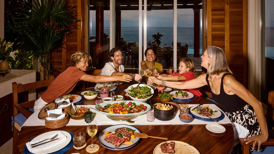 Family of five toasting at a table full of colourful dishes