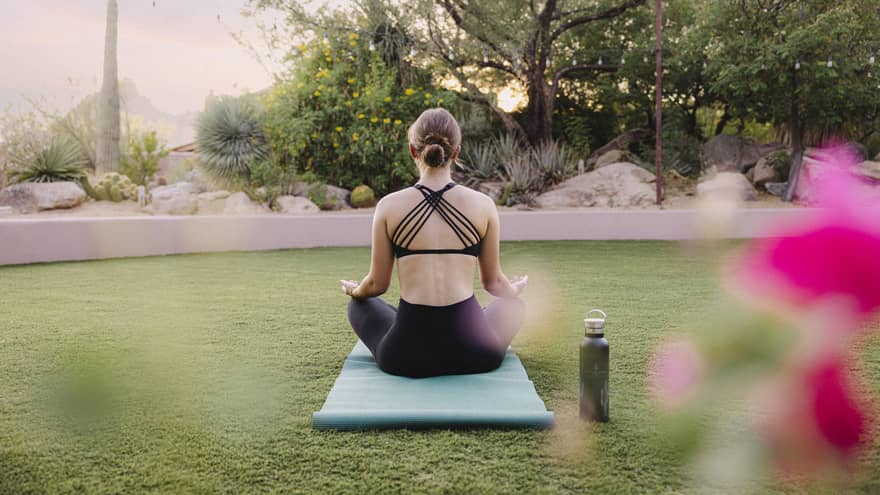 Person doing yoga outside on a blue yoga mat with a water bottle beside them.