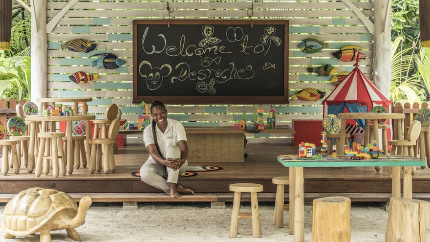 Kids Club play area with chalkboard, fish accents and tables, and a smiling staff member seated