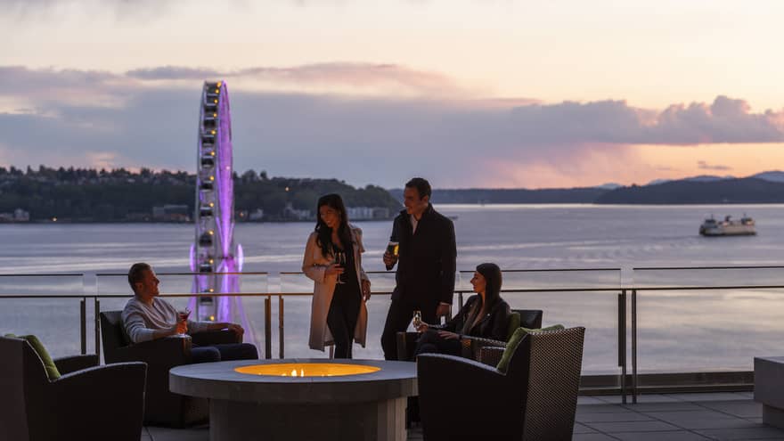 Group on the patio at Four Seasons Hotel Seattle at sunset, with Elliott Bay, the Great Wheel and a ferry in background