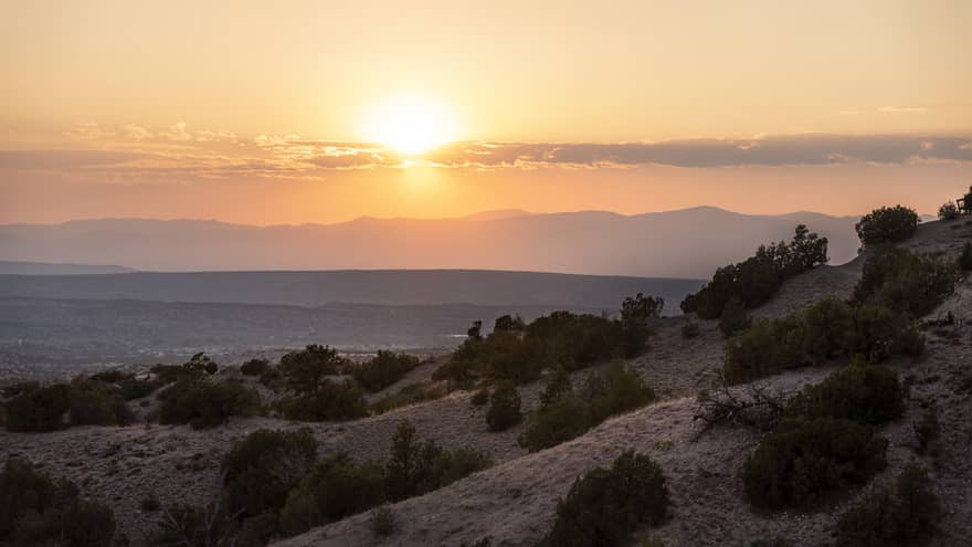 A hill with small trees with the sun setting behind it.